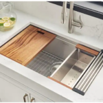 Kitchen workstation sink with walnut cutting board and drying rack on marble countertop