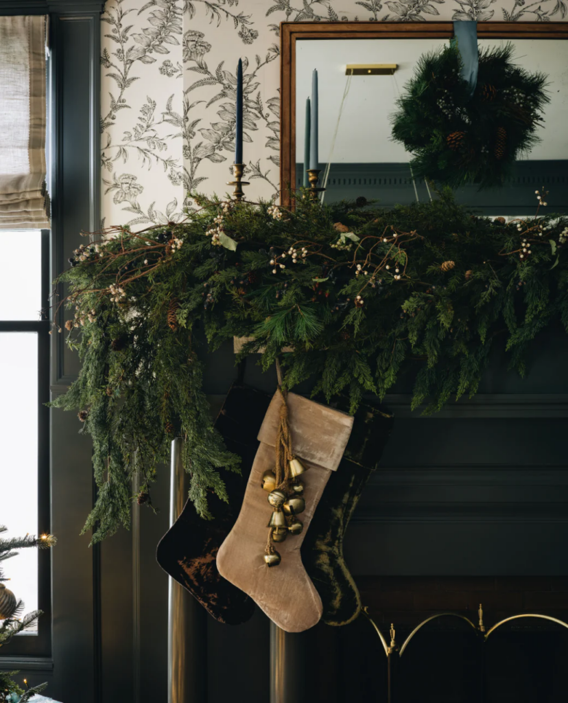 Christmas mantel with green garland, velvet stockings and hanging bells