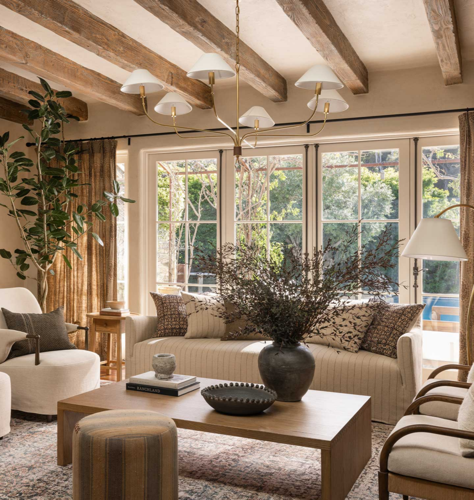 neutral living room with sofa and accent chairs, wood beam ceiling and large windows. plant accents and neutral pattern throw pillows on sofa.