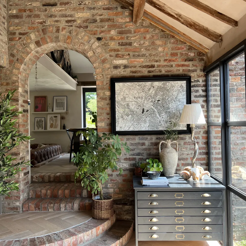 brick wall entry with vaulted, beam ceiling. black console table with accessories and plants.