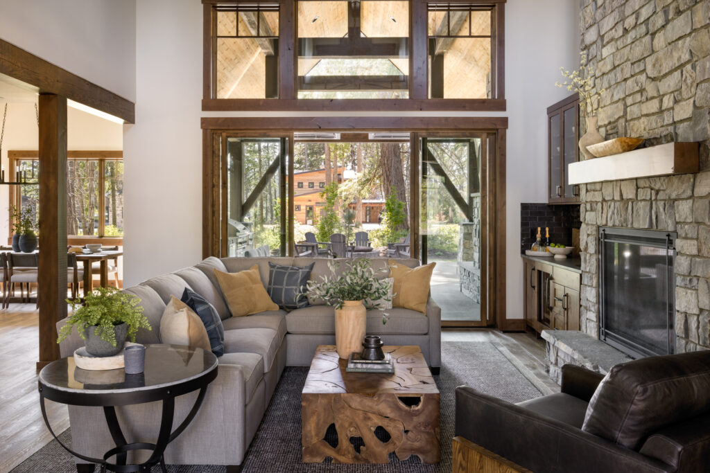 Open plan great room in Suncadia mountain vacation house by Michelle Yorke Interior Design. Features a raw stone fireplace, view of the outdoor patio, a neutral sectional with accent pillows and organic wood coffee table.